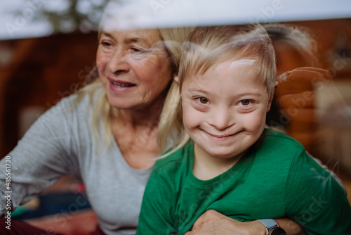 Boy with Down syndrome with his grandmother looking at camera through window at home. photo