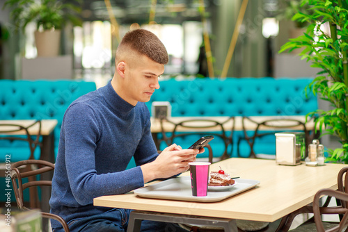 Young man works online. In the hands of a smartphone, gadgets for working on the Internet. A man in a cafe reads the news and works using the phone. 