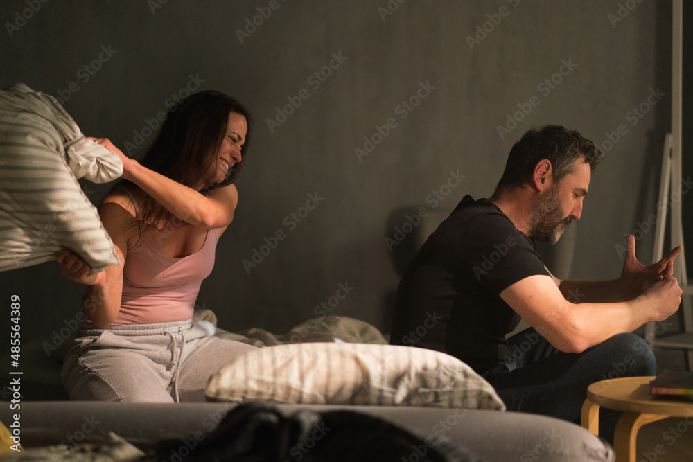 Obraz premium Jealous betrayed woman beating her husband with pillow in bed, relationship problems concept.