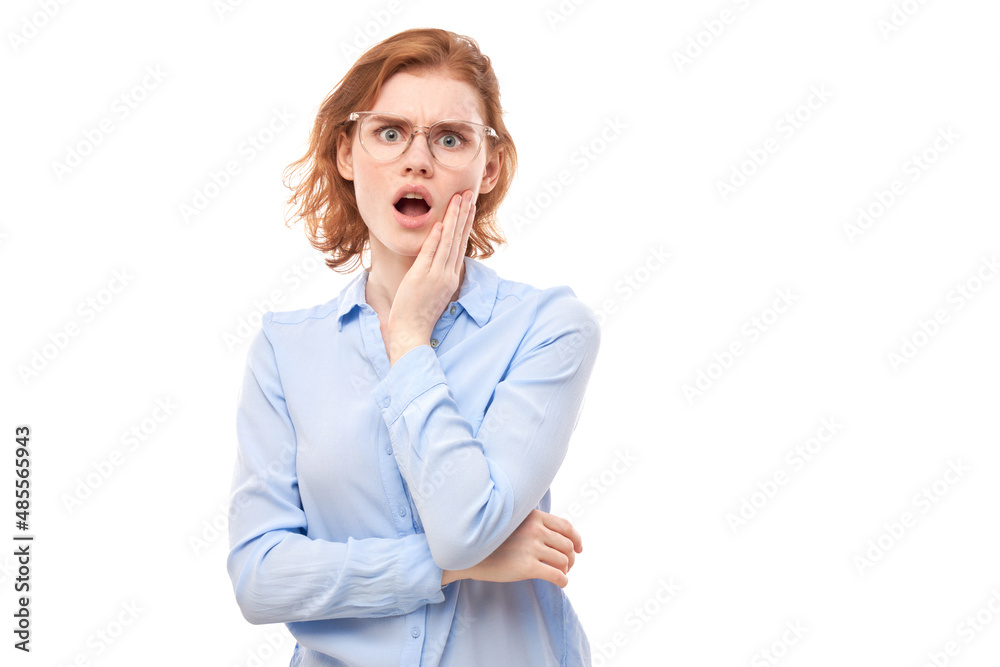 Shocked face ginger girl in business shirt looks surprised with open mouth holding head with hands on white studio background Shocked face ginger girl in business shirt looks surprised with open mouth holding head with hands on white studio background