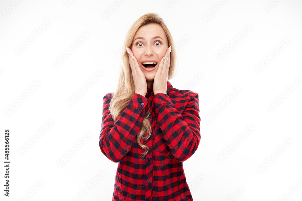 Fototapeta premium Shocked blond girl looks surprised holding head with hands on white studio background with copy space