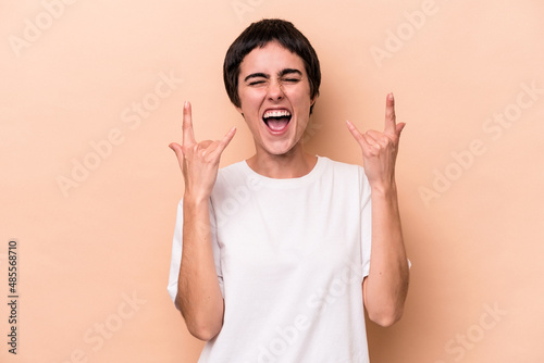 Photos Young caucasian woman isolated on beige background showing a horns gesture as a revolution concept