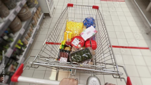 First-person view of puttig groceries in shopping cart. Female wearing yellow sweater at a grocceries store putting food into shopping cart