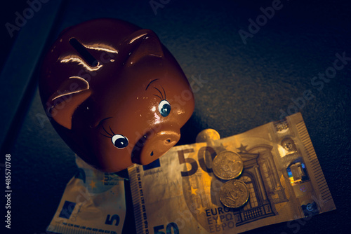 Red piggy bank stands in a dark gray kitchen sink with money around