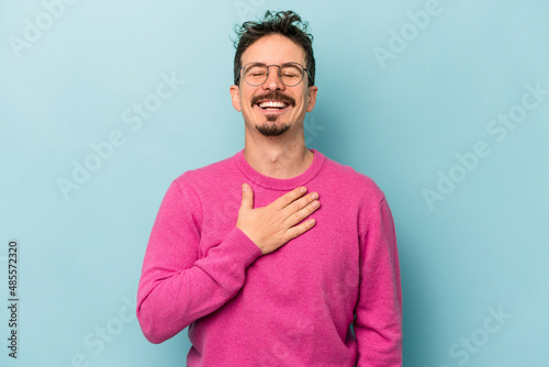 Young caucasian man isolated on blue background laughs out loudly keeping hand on chest.