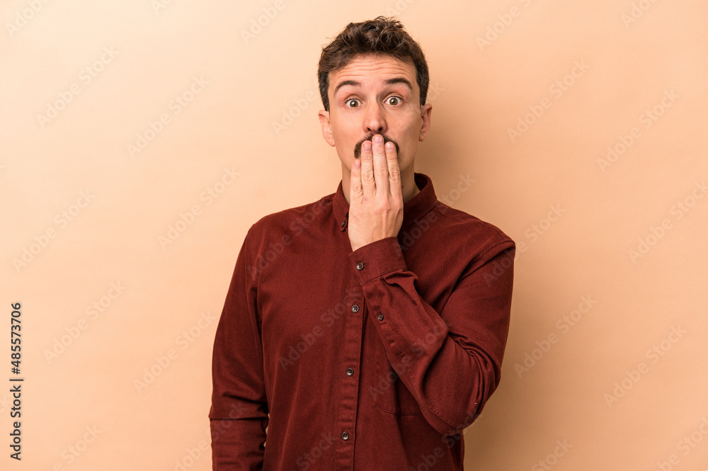 Young caucasian man isolated on beige background shocked, covering mouth with hands, anxious to discover something new. Young caucasian man isolated on beige background shocked, covering mouth with hands, anxious to discover something new.