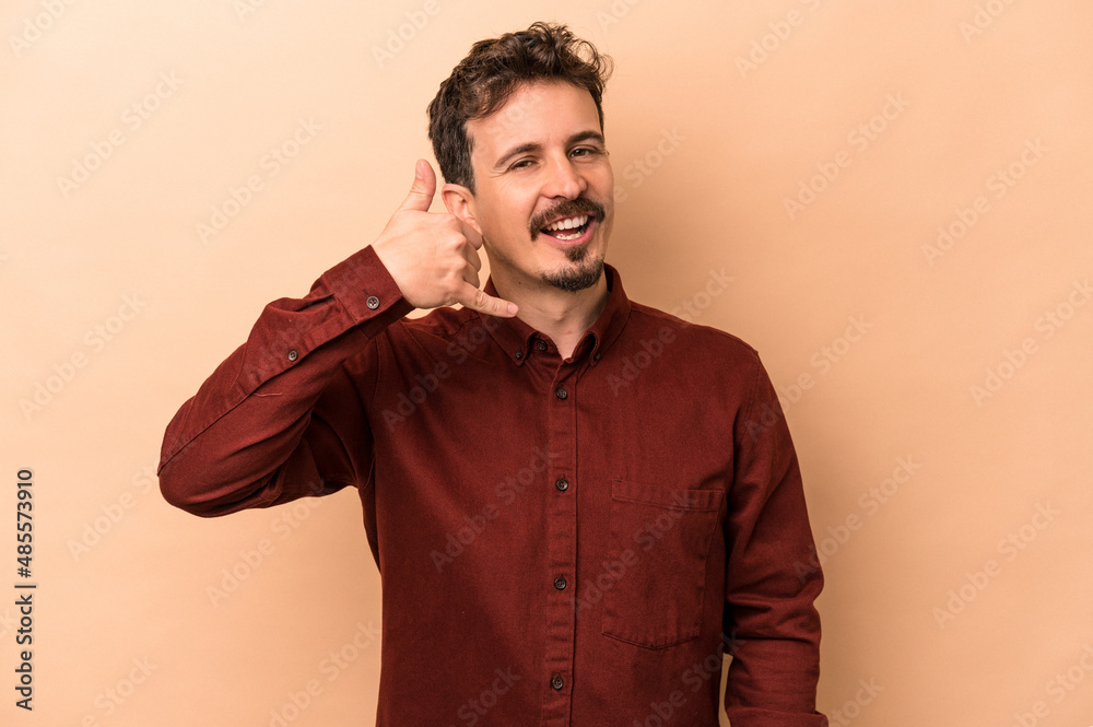 Young caucasian man isolated on beige background showing a mobile phone call gesture with fingers. Young caucasian man isolated on beige background showing a mobile phone call gesture with fingers.