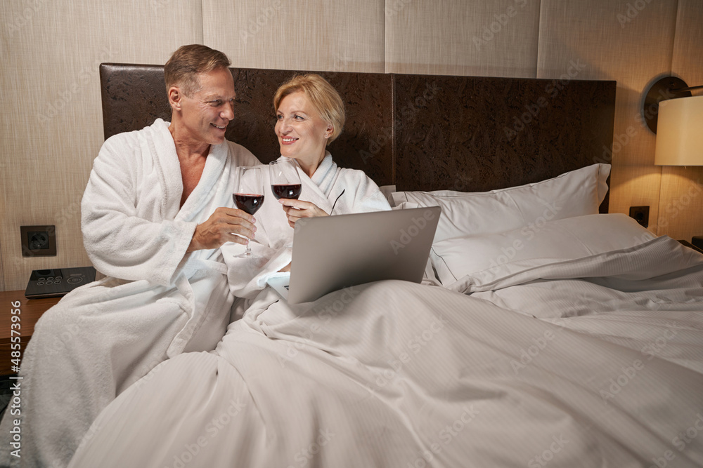 Obraz premium Excited lady and her boyfriend enjoying wine in hotel bed