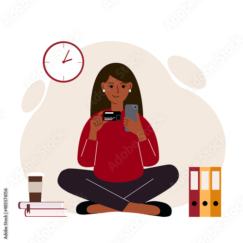 A woman sits cross-legged with a mobile phone in one hand and a bank card in the other. Concept of online credit