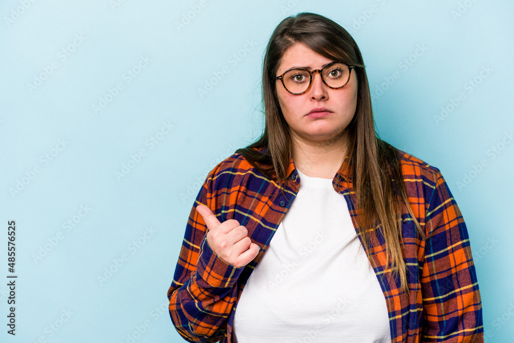 Young caucasian overweight woman isolated on blue background shocked pointing with index fingers to a copy space.