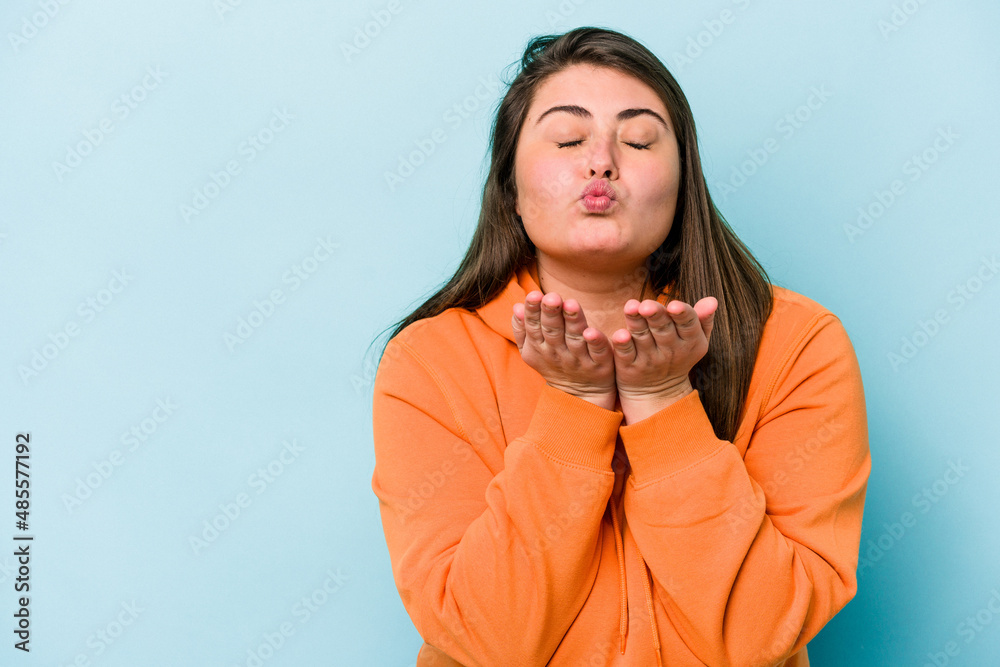Young caucasian overweight woman isolated on blue background folding lips and holding palms to send air kiss. Young caucasian overweight woman isolated on blue background folding lips and holding palms to send air kiss.