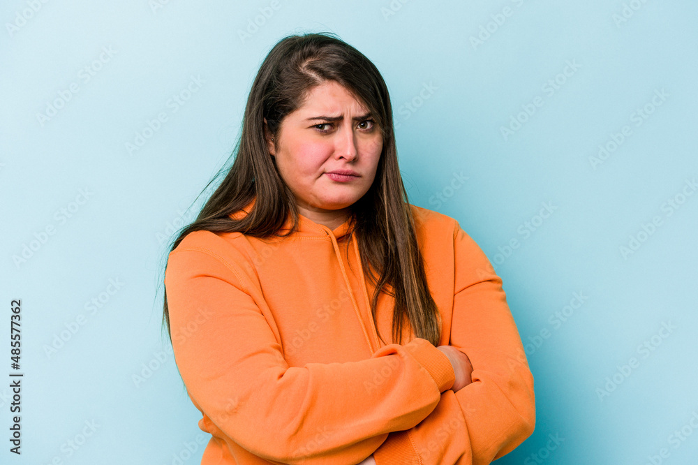 Young caucasian overweight woman isolated on blue background suspicious, uncertain, examining you.