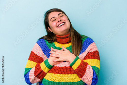 Young caucasian overweight woman isolated on blue background laughing keeping hands on heart, concept of happiness.