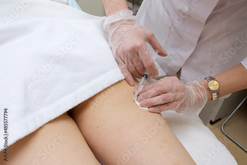 Cosmetologist conducts a session of mesotherapy making an injection in the patient s leg