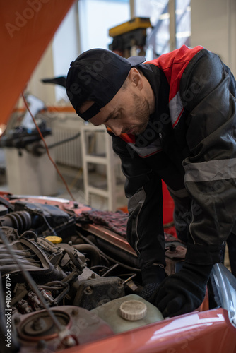 Vertical portrait of male mechanic looking under hood while repairing car in auto shop