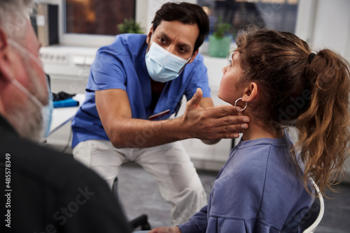 Male doctor examining girl patient's neck during appointment photo