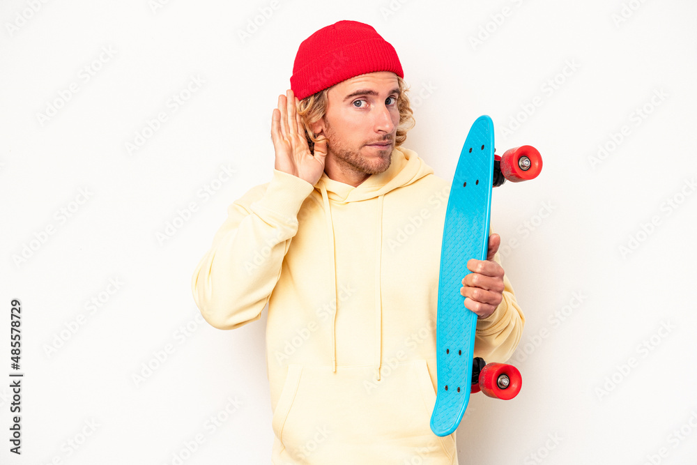 Young skater caucasian man isolated on white background trying to listening a gossip.