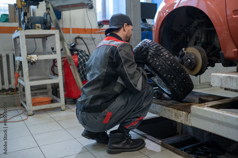 Full length portrait of male mechanic changing tires on car while working in auto repair shop, copy space Full length portrait of male mechanic changing tires on car while working in auto repair shop, copy space