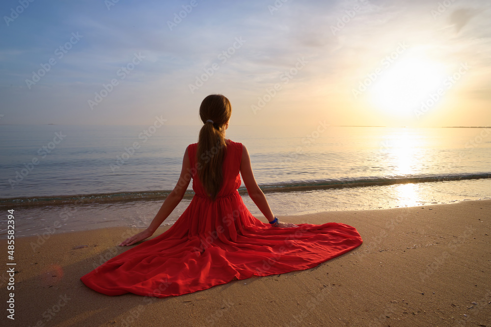 Young happy woman in red dress relaxing on sandy beach by seaside enjoying warm tropical morning Young happy woman in red dress relaxing on sandy beach by seaside enjoying warm tropical morning