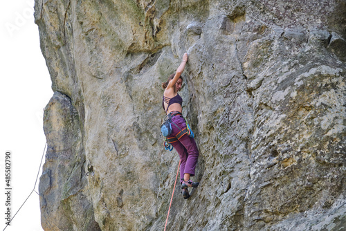 Young woman climbing steep wall of rocky mountain. Girl climber overcomes challenging route. Engaging in extreme sport concept