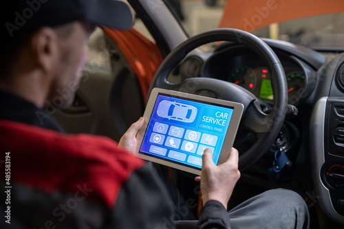 Close up of car mechanic using digital tablet with service and maintenance app on screen while inspecting vehicle in auto repair shop