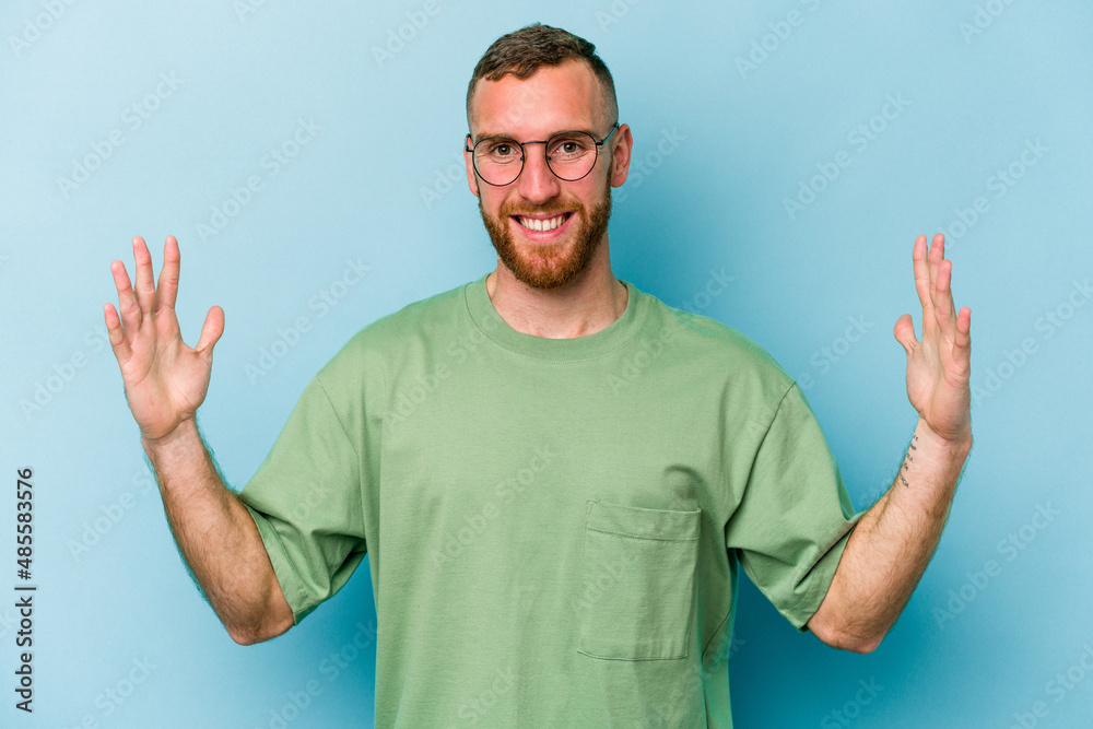 Naklejka premium Young caucasian man isolated on blue background holding something little with forefingers, smiling and confident.