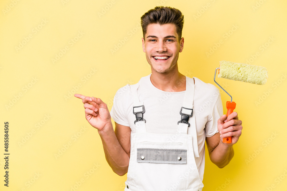 Young painter man isolated on yellow background smiling and pointing aside, showing something at blank space. Young painter man isolated on yellow background smiling and pointing aside, showing something at blank space.