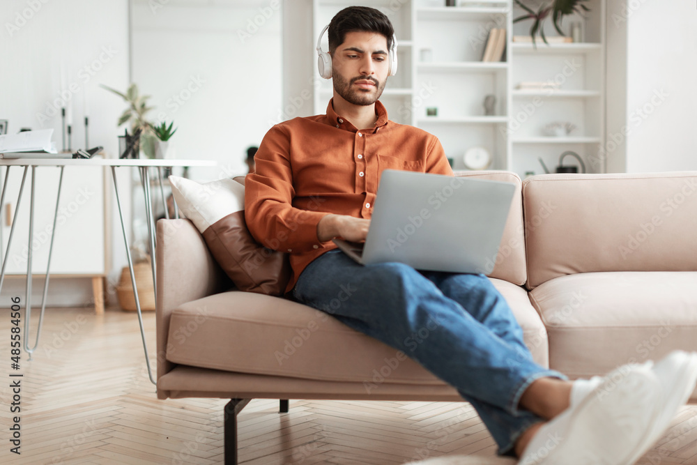 Focused Arab man in headphones using pc at home Focused Arab man in headphones using pc at home