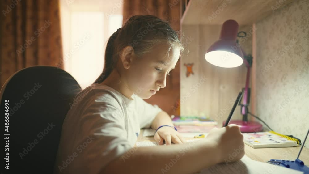 Education concept. Cute smart school child girl writing doing homework sit at home table. Teen girl doing school assignment. Happy child studying at home in the evening. Education concept. Cute smart school child girl writing doing homework sit at home table. Teen girl doing school assignment. Happy child studying at home in the evening.