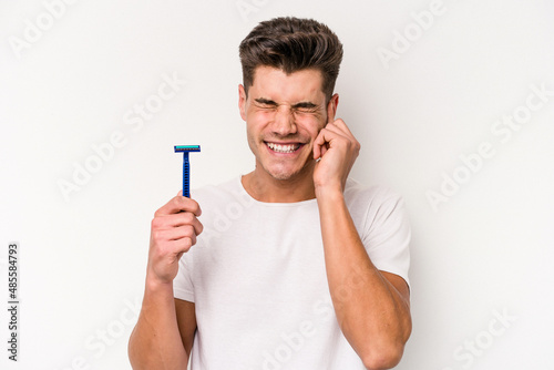 Young caucasian man shaving his beard isolated on white background covering ears with hands.