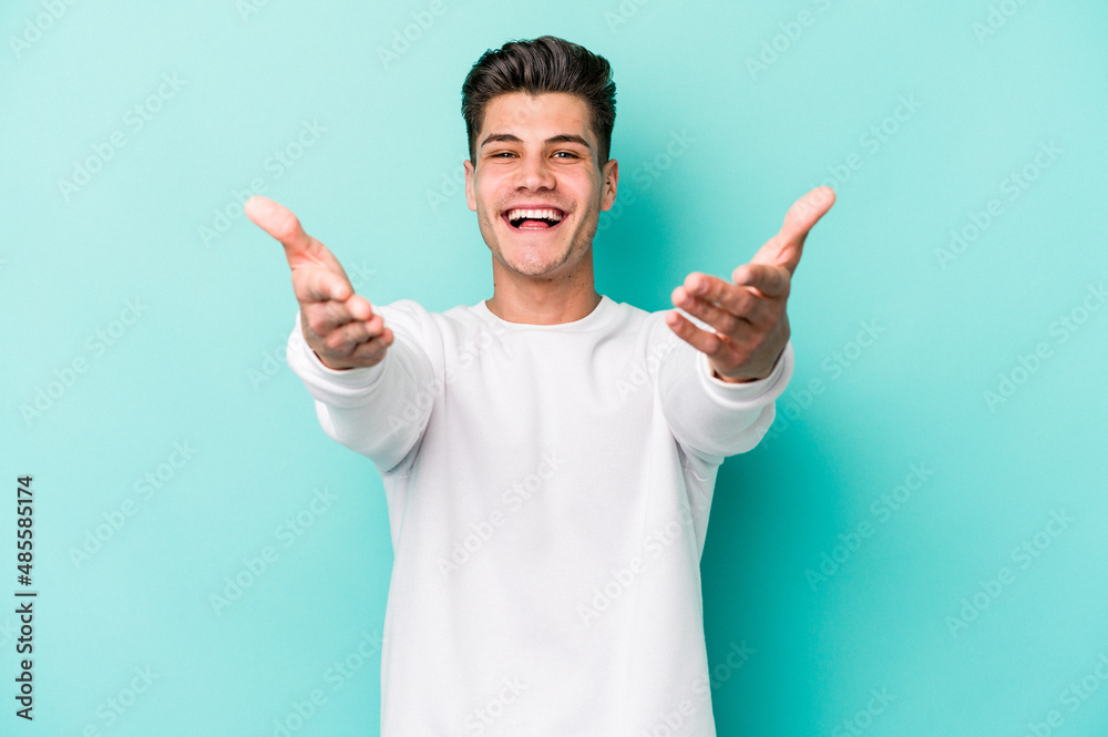 Young caucasian man isolated on blue background feels confident giving a hug to the camera.