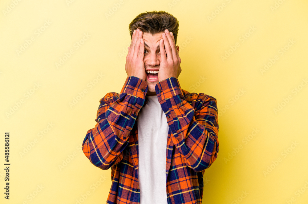 Young caucasian man isolated on yellow background having fun covering half of face with palm.