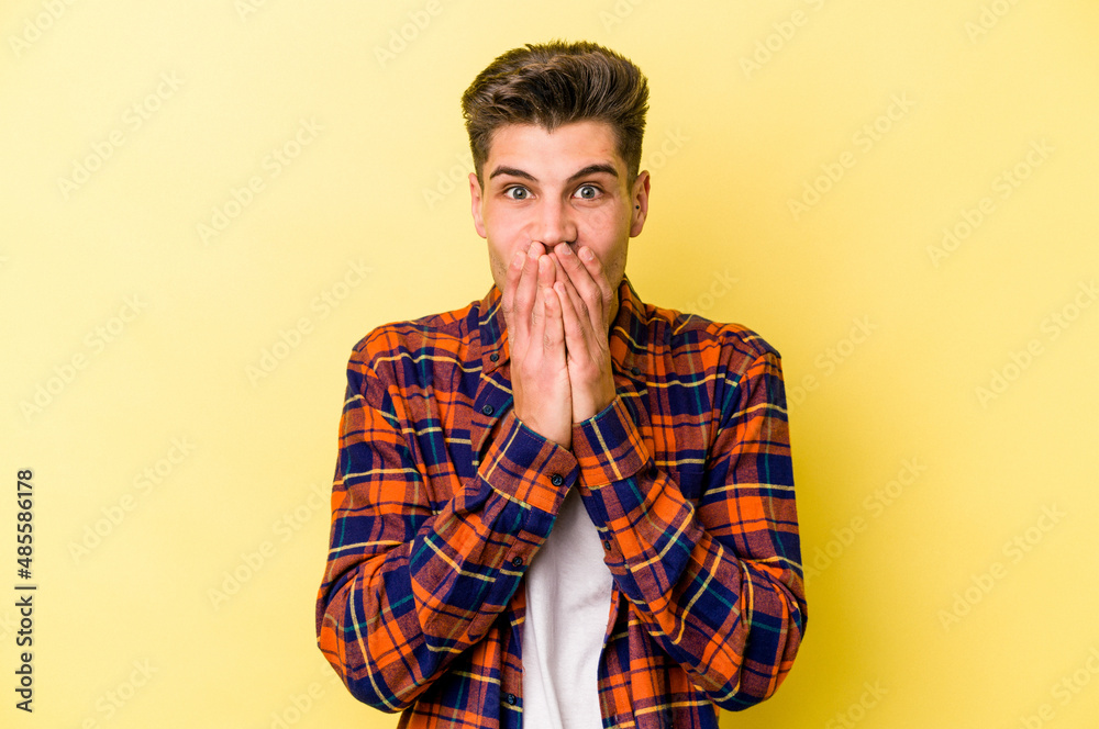 Young caucasian man isolated on yellow background shocked covering mouth with hands. Young caucasian man isolated on yellow background shocked covering mouth with hands.