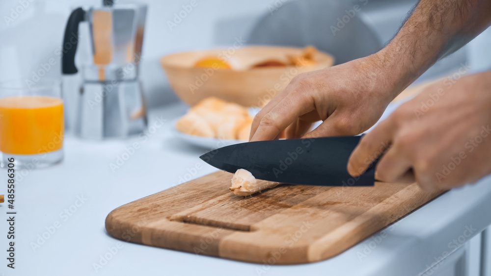 partial view of man cutting banana on chopping board in kitchen