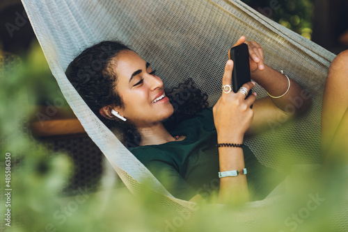 Foto Beautiful brunette woman with laughing hair resting in a hammock with her cell phone and wireless headphones