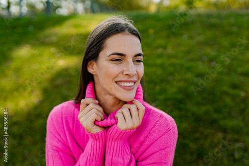 young smiling woman in pink sweater walking in green park