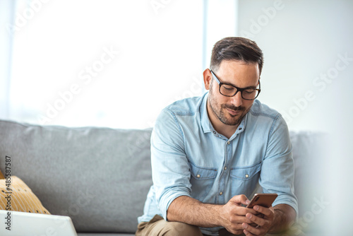 A serious young man working from home using a smartphone and notebook computer, male hands using a smartphone inside, a man at his workplace using technology. New normality concept photo