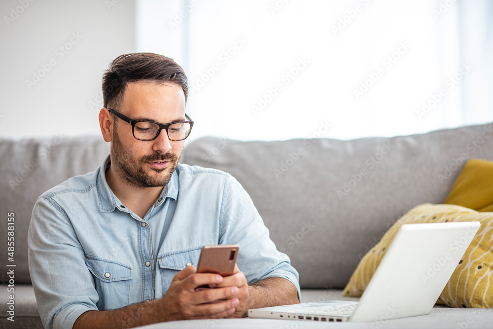 A serious young man working from home using a smartphone and notebook computer, male hands using a smartphone inside, a man at his workplace using technology. New normality concept A serious young man working from home using a smartphone and notebook computer, male hands using a smartphone inside, a man at his workplace using technology. New normality concept