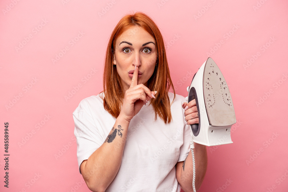 Young caucasian woman holding iron isolated on pink background keeping a secret or asking for silence. Young caucasian woman holding iron isolated on pink background keeping a secret or asking for silence.