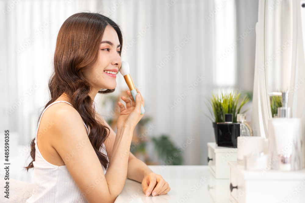 Smiling of young beautiful pretty asian woman clean fresh healthy white skin looking at mirror.asian girl holding make-up brushes and make up on face with cosmetics set at home.facial beauty