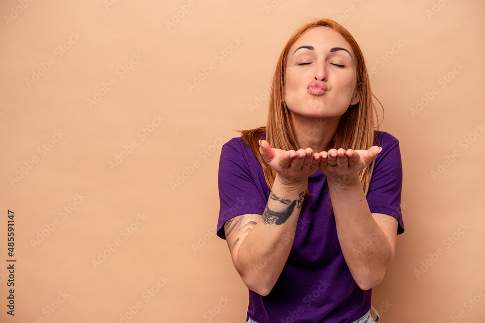 Young caucasian woman isolated on beige background folding lips and holding palms to send air kiss. Young caucasian woman isolated on beige background folding lips and holding palms to send air kiss.