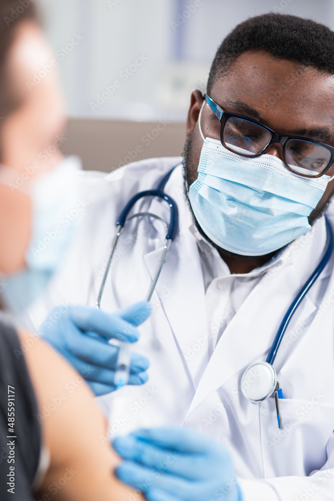 African-American doctor makes a coronavirus vaccine using a syringe and hypodermic needle. Professional medical worker and patient at the hospital office. Vaccination and safety. African-American doctor makes a coronavirus vaccine using a syringe and hypodermic needle. Professional medical worker and patient at the hospital office. Vaccination and safety.