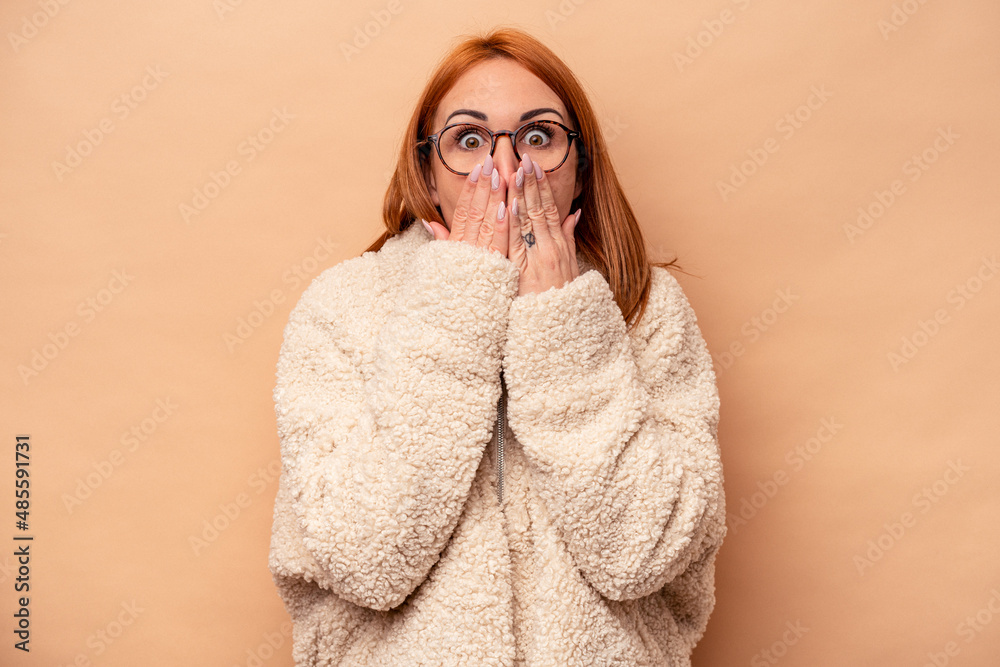 Young caucasian woman isolated on beige background shocked, covering mouth with hands, anxious to discover something new. Young caucasian woman isolated on beige background shocked, covering mouth with hands, anxious to discover something new.