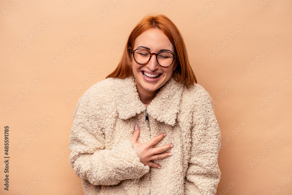 Young caucasian woman isolated on beige background laughs out loudly keeping hand on chest.