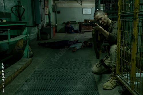 Fotografie, Tablou Full length portrait of tough female soldier pointing gun at camera in dark indu