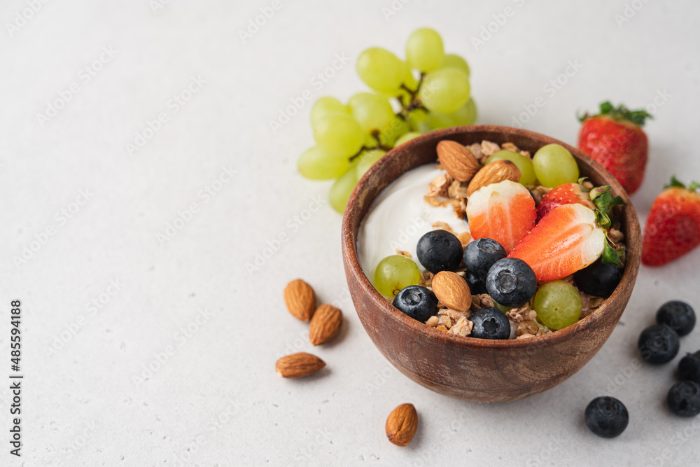Greek yogurt with berries and granola in wooden bowl. Healthy breakfast with strawberries, grapes, blueberries, oatmeal and almonds