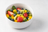 Pieces of mango, strawberries, blueberries, kiwi and mint in white bowl. Fruity fresh raw summer salad