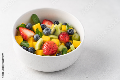 Pieces of mango  strawberries  blueberries  kiwi and mint in white bowl. Fruity fresh raw summer salad