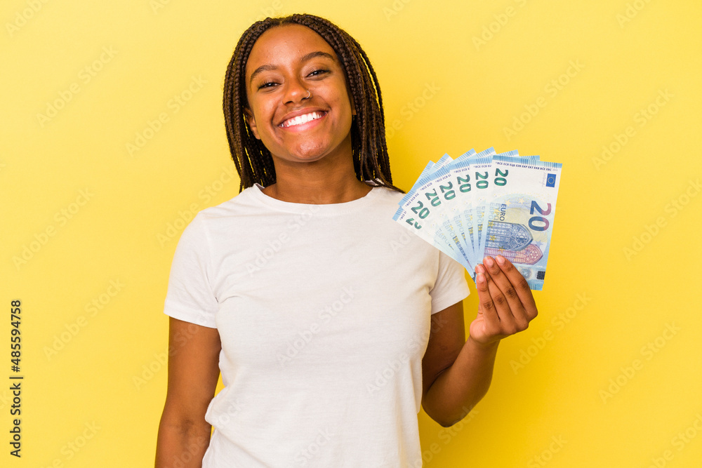Young african American woman holding bills isolated on yellow background happy, smiling and cheerful. Young african American woman holding bills isolated on yellow background happy, smiling and cheerful.