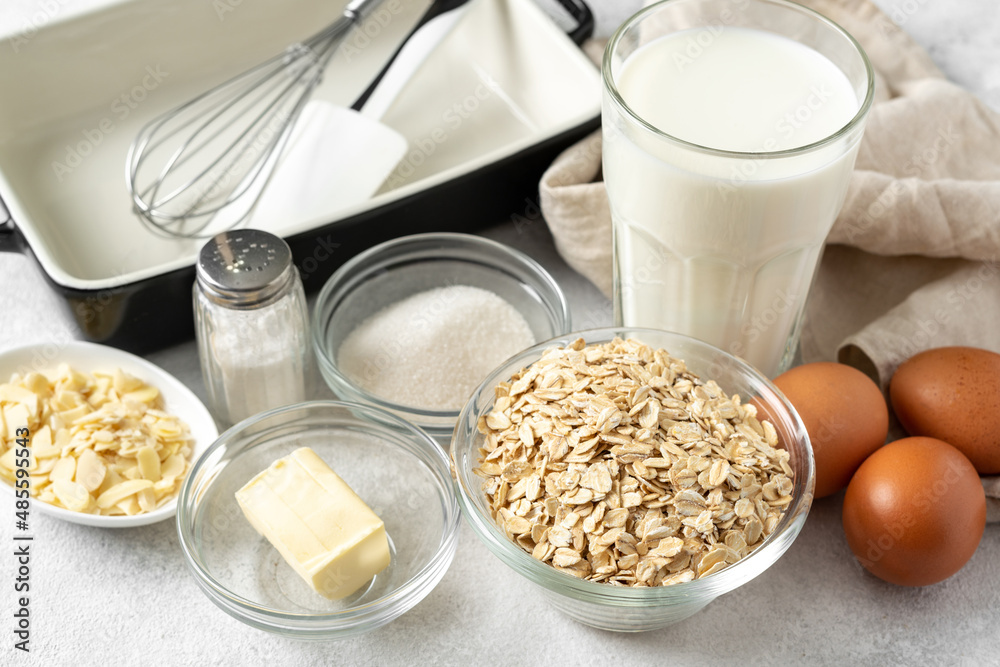 Ingredients for pudding or oatmeal pie on a light gray culinary background. Eggs, cereals, almonds, sugar, milk and butter on the kitchen table Ingredients for pudding or oatmeal pie on a light gray culinary background. Eggs, cereals, almonds, sugar, milk and butter on the kitchen table